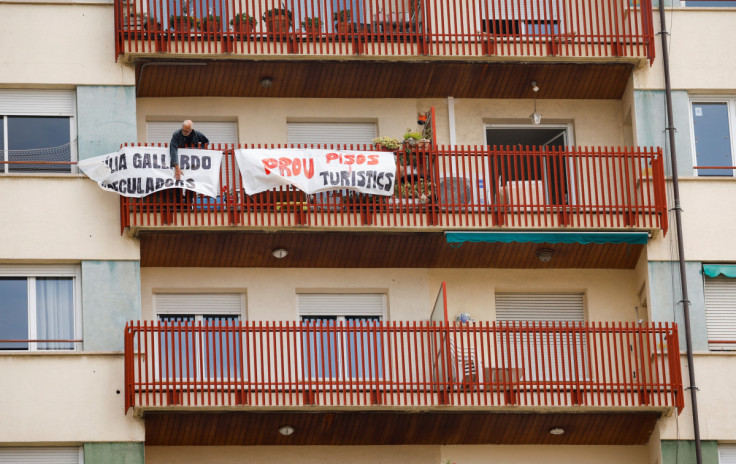 Un hombre ata pancartas de protesta en el balcón de un edificio recientemente convertido para uso turístico en el barrio de Sants en Barcelona