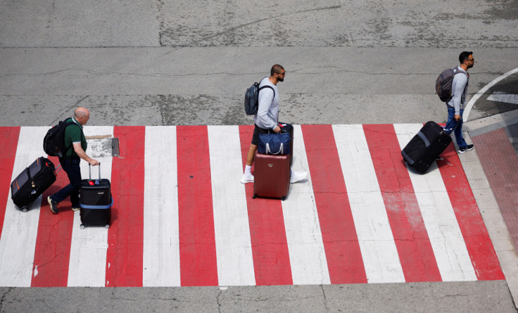 Personas con maletas caminan por un paso de peatones junto a una terminal de cruceros en el Puerto de Barcelona